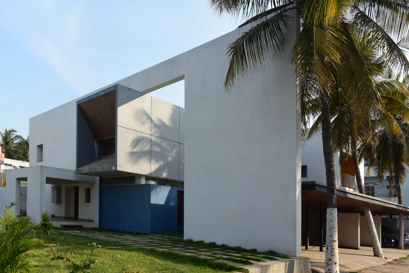 A white residence with a framed upper volume among coconut palms